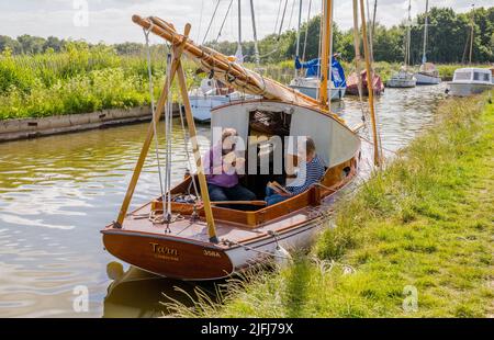 Ein älteres Paar vertäute in Horsley Mere und las auf einem traditionellen Norfolk Broads klassischen Segelboot. Stockfoto