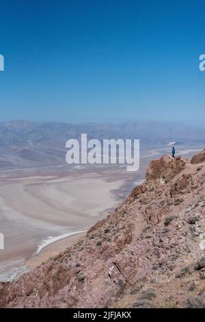 Ein Mann blickt vom Dante's Peak Wanderweg über das Death Valley Becken und betrachtet die dramatische Landschaft in einem inspirierenden Solo-Wanderfoto. Stockfoto