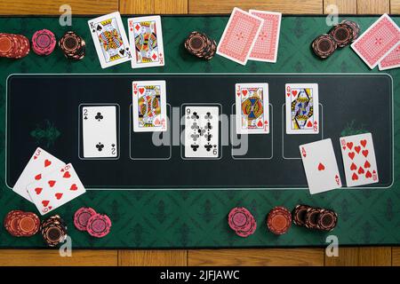 Blick auf eine königliche gerade bündig gewinnende Hand auf einem Poker texas Hold'em Spielmatte mit Glücksspiel Chip Stacks, Spielkarten und gefalteten Händen Stockfoto