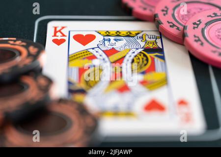 Nahaufnahme eines Königs der Herzen, der Karten spielt und Poker-Wetten-Chips auf einer Pokermatte setzt. Konzept - Poker-Strategie, Glücksspiel, Wetten, Spielsucht Stockfoto