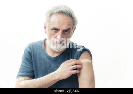Senior grauhaarige Mann zeigt berührt Arm mit einem Patch auf und schaut auf die Kamera-Studio gefilmt isoliert Kopie Raum drinnen . Hochwertige Fotos Stockfoto
