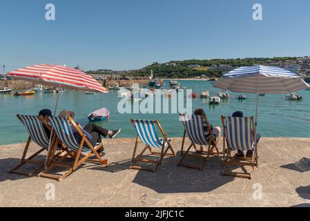 St Ives, Cornwall, England, Großbritannien. 2022. Urlauber entspannen sich in Liegestühlen am Hafen mit Blick auf den Porthminster Beach. St. Ives berühmte Holida Stockfoto