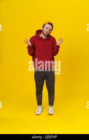 Ich KENNE EINEN hübschen jungen Mann nicht, der in legerer Kleidung gestikuliert ist, mit hochgesteckten Händen und Blick auf die Kamera auf gelbem Hintergrund. Hipster Mode bärtig smart Mann casual Look. Stockfoto