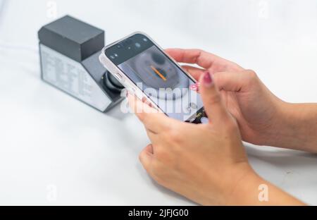 Weibliche Hand hält Smartphone für ein Foto mit dem RI eines Refraktometers, um die Art von Schmuck zu bestätigen. Stockfoto