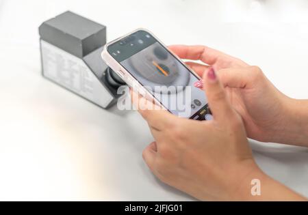 Weibliche Hand hält Smartphone für ein Foto mit dem RI eines Refraktometers, um die Art von Schmuck zu bestätigen. Stockfoto