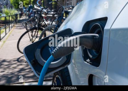 Elektroauto in Amsterdam eingesteckt und neben Fahrrädern geladen Stockfoto