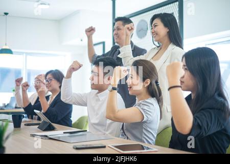 Eine Gruppe glücklicher asiatischer Geschäftsleute, die lächeln und die Fäuste hoch halten. Seitenansicht. Stockfoto
