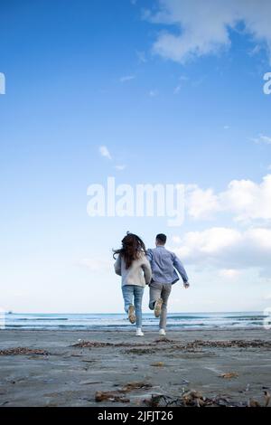Junges Paar von hinten läuft am Strand zum Meer in Larnaca, Zypern Stockfoto