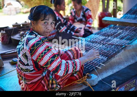 Koronadal, PH - 16. Juli 2016: Einer der ausgewählten Dreamweavers (ein T'boli T'nalak-Meisterweber), der traditionelle Kleidung trägt, webt Muster in Textilien Stockfoto