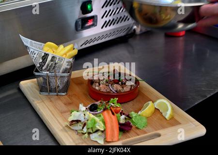 Serviert in einem Ramekin auf einem Holzbrett mit Salat und pommes frites Stockfoto
