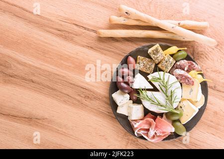Wurstplatte am Holztisch: Auswahl an Käse und Fleischsnacks, serviert mit Oliven und Kräutern. Italienische Antipasti zum Aperitif. Speisekarte im Restaurant Stockfoto