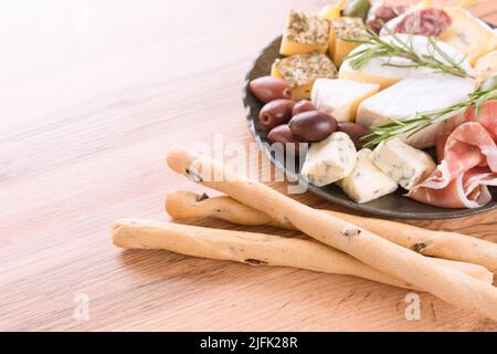 Wurstplatte am Holztisch: Auswahl an Käse und Fleischsnacks, serviert mit Oliven und Grissini-Brotstäbchen. Italienische Antipasti zum Aperitif. Stockfoto