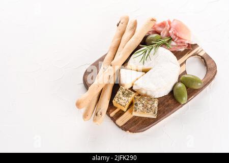 Wurstplatte am weißen Tisch: Auswahl an Käse und Fleischsnacks, serviert mit Oliven und Grissini-Brotscheiben. Italienische Antipasti zum Aperitif. Stockfoto