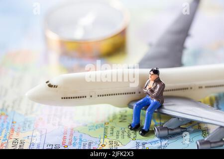 Miniaturmenschen: Geschäftsmann, der auf einem Flugzeugflügel sitzt, um die Welt mit Wort Karte und Kompass Hintergrund zu reisen.Erde Hintergrund Konzept. Stockfoto