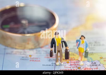 Miniaturmenschen, die auf der Weltkarte stehen, mit verschwommenem Kompass-Hintergrund. Business- und Reisekonzept. Stockfoto