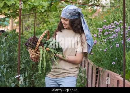 Junge Bäuerin lächelt mit einem Haufen Gemüse in einem Weidenkorb. Stockfoto