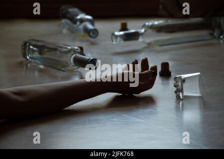 Die Hand einer Frau liegt auf dem Boden und daneben ist eine Flasche und ein Glas in einer Wohnung im Dunkeln, Alkoholismus und Trinken, eine schlechte Angewohnheit, weibliche Alco Stockfoto