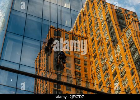 Waschmaschinen waschen Wolkenkratzerfenster, die auf hängenden Sitzen sitzen. Stockfoto