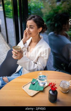 Junge Geschäftsfrau, die Kaffee im Straßencafé in der Stadt hält und trinkt. Portrait einer schönen Arbeiterin, die auf der Straße in Prag wartet Stockfoto