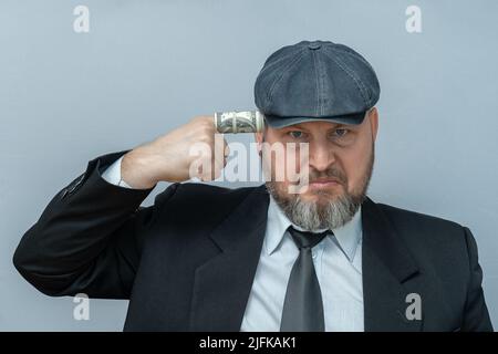 Der Mann legte seinen Finger in seinen Tempel. Der Finger ist in eine Dollarnote gewickelt. Er sieht aus, als wolle er sich selbst erschießen. Stockfoto