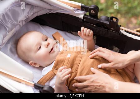 Foto von süßen niedlichen Mutter kleine Tochter tragen lässige Outfits Wandern Reiten Baby Kutsche außerhalb Garten Stockfoto