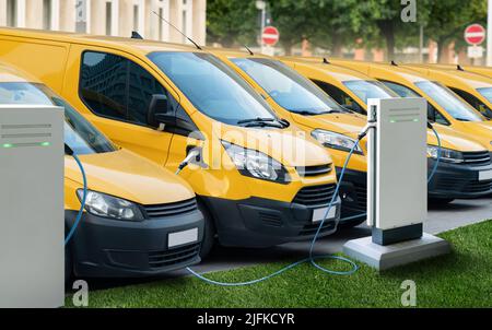 Reihe gelber elektrischer Lieferwagen an Ladestationen für Elektrofahrzeuge Stockfoto