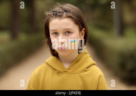 Das Gesicht eines verängstigten Mädchens, gemalt auf ihre Wange in den gelb-blauen Farben der ukrainischen Flagge, eine Bitte um Hilfe. Kinder bitten um Frieden. Hoch Stockfoto