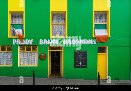 Blick auf einen typisch irischen Pub mit einer grünen und gelben façade, mit der irischen Flagge in der Stadt Dingle. Stockfoto