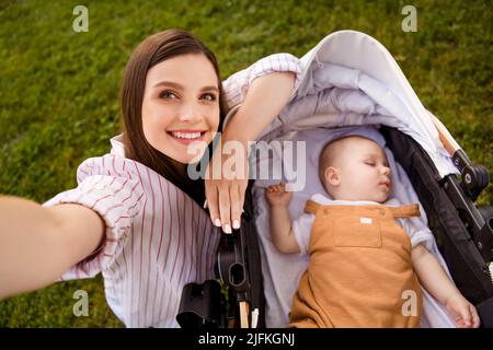 Foto von charmanten niedlichen positiven Mama Blogger gehen schlafen Kleinkind Kinderwagen machen Selfie-Porträt draußen Stockfoto