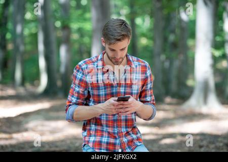Junger, gutaussehender Mann im karierten Hemd plaudert draußen am Telefon Stockfoto