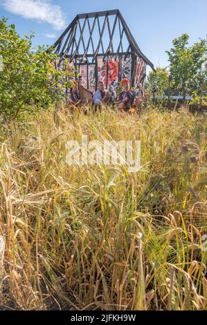 Hampton Court Palace, Surrey, Großbritannien. 4. Juli 2022. RHS Hampton Court Palace Garden Festival Pressetag für die größte Blumenschau der Welt, die bis zum 9. Juli 2022 stattfindet. Bild: Global Impact Garden: Traditionelle ukrainische Band tritt hinter Weizenfeldern auf dem von Victoria Manoylo und Carrie Preston entworfenen „What does Not Burn Garden“ auf, einer Destillation der ukrainischen Landschaft und Kultur. Es zeigt den Rushnyk, ein besticktes Tuch, das in vielen Ritualen verwendet wird, als Symbol des Lebens und der Identität. Wie eine neue Haut schmücken Rushnyks die Überreste einer verbrannten Hütte, die als Silhouette in der Landschaft steht. Kredit: Ma Stockfoto