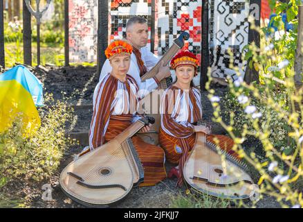 Hampton Court Palace, Surrey, Großbritannien. 4. Juli 2022. RHS Hampton Court Palace Garden Festival Pressetag für die größte Blumenschau der Welt, die bis zum 9. Juli 2022 stattfindet. Bild: Global Impact Garden: Traditionelle ukrainische Band tritt hinter Weizenfeldern auf dem von Victoria Manoylo und Carrie Preston entworfenen „What does Not Burn Garden“ auf, einer Destillation der ukrainischen Landschaft und Kultur. Es zeigt den Rushnyk, ein besticktes Tuch, das in vielen Ritualen verwendet wird, als Symbol des Lebens und der Identität. Wie eine neue Haut schmücken Rushnyks die Überreste einer verbrannten Hütte, die als Silhouette in der Landschaft steht. Kredit: Ma Stockfoto