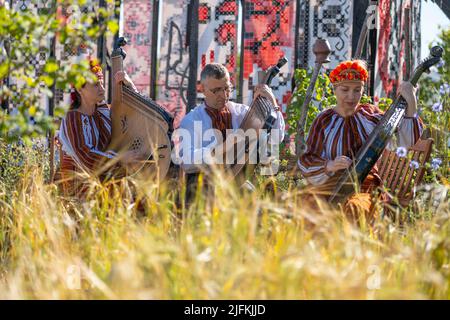 Hampton Court Palace, Surrey, Großbritannien. 4. Juli 2022. RHS Hampton Court Palace Garden Festival Pressetag für die größte Blumenschau der Welt, die bis zum 9. Juli 2022 stattfindet. Bild: Global Impact Garden: Traditionelle ukrainische Band tritt hinter Weizenfeldern auf dem von Victoria Manoylo und Carrie Preston entworfenen „What does Not Burn Garden“ auf, einer Destillation der ukrainischen Landschaft und Kultur. Es zeigt den Rushnyk, ein besticktes Tuch, das in vielen Ritualen verwendet wird, als Symbol des Lebens und der Identität. Wie eine neue Haut schmücken Rushnyks die Überreste einer verbrannten Hütte, die als Silhouette in der Landschaft steht. Kredit: Ma Stockfoto