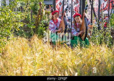 Hampton Court Palace, Surrey, Großbritannien. 4. Juli 2022. RHS Hampton Court Palace Garden Festival Pressetag für die größte Blumenschau der Welt, die bis zum 9. Juli 2022 stattfindet. Bild: Global Impact Garden: Traditionelle ukrainische Band tritt hinter Weizenfeldern auf dem von Victoria Manoylo und Carrie Preston entworfenen „What does Not Burn Garden“ auf, einer Destillation der ukrainischen Landschaft und Kultur. Es zeigt den Rushnyk, ein besticktes Tuch, das in vielen Ritualen verwendet wird, als Symbol des Lebens und der Identität. Wie eine neue Haut schmücken Rushnyks die Überreste einer verbrannten Hütte, die als Silhouette in der Landschaft steht. Kredit: Ma Stockfoto