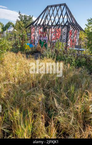 Hampton Court Palace, Surrey, Großbritannien. 4. Juli 2022. RHS Hampton Court Palace Garden Festival Pressetag für die größte Blumenschau der Welt, die bis zum 9. Juli 2022 stattfindet. Bild: Global Impact Garden: Traditionelle ukrainische Band tritt hinter Weizenfeldern auf dem von Victoria Manoylo und Carrie Preston entworfenen „What does Not Burn Garden“ auf, einer Destillation der ukrainischen Landschaft und Kultur. Es zeigt den Rushnyk, ein besticktes Tuch, das in vielen Ritualen verwendet wird, als Symbol des Lebens und der Identität. Wie eine neue Haut schmücken Rushnyks die Überreste einer verbrannten Hütte, die als Silhouette in der Landschaft steht. Kredit: Ma Stockfoto