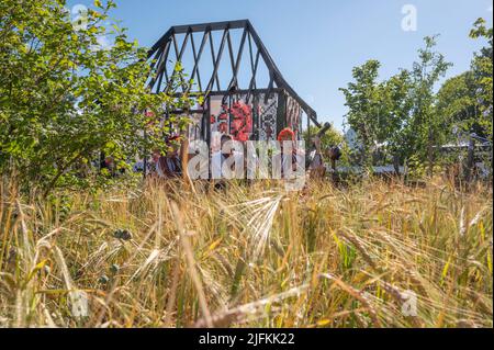 Hampton Court Palace, Surrey, Großbritannien. 4. Juli 2022. RHS Hampton Court Palace Garden Festival Pressetag für die größte Blumenschau der Welt, die bis zum 9. Juli 2022 stattfindet. Bild: Global Impact Garden: Traditionelle ukrainische Band tritt hinter Weizenfeldern auf dem von Victoria Manoylo und Carrie Preston entworfenen „What does Not Burn Garden“ auf, einer Destillation der ukrainischen Landschaft und Kultur. Es zeigt den Rushnyk, ein besticktes Tuch, das in vielen Ritualen verwendet wird, als Symbol des Lebens und der Identität. Wie eine neue Haut schmücken Rushnyks die Überreste einer verbrannten Hütte, die als Silhouette in der Landschaft steht. Kredit: Ma Stockfoto