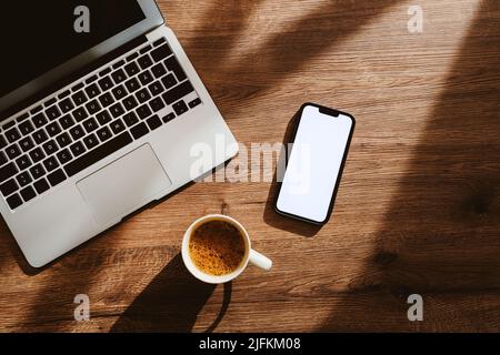 Tasse Kaffee, Laptop-Computer und Smartphone mit leerem weißen Mockup-Bildschirm auf dem Schreibtisch des Heimbüros, Flachlagerung von oben Stockfoto