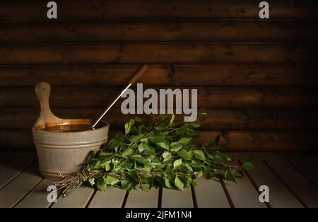 Eine schwach beleuchtete Szene mit einem traditionellen finnischen Badebesen, der in einer Sauna auf die Badegäste wartet und für einen entspannenden, reinigenden Moment bereit ist. Stockfoto