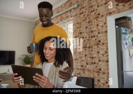 Lächelndes junges multiethnisches Paar, das zu Hause ein Tablet benutzt Stockfoto