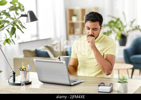 Kranker indischer Mann mit Laptop, der im Heimbüro hustet Stockfoto