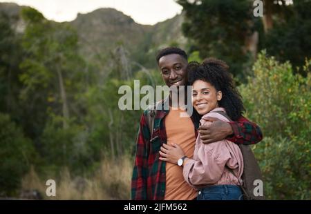 Lächelndes junges multiethnisches Paar, das Arm in Arm auf einem Wanderweg steht Stockfoto