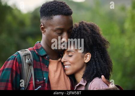 Liebevolles junges multiethnisches Paar, das sich während einer Pause von einer Wanderung umarmt Stockfoto