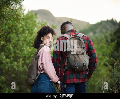 Lächelndes junges multiethnisches Paar, das Hand in Hand im Freien wandert Stockfoto