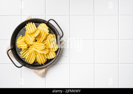 Wellige leicht gesalzene Kartoffelchips auf weißem quadratischen Keramiktischhintergrund, Draufsicht flach liegend, mit Kopierraum für Text Stockfoto