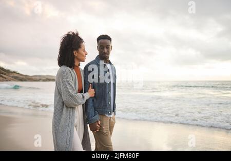 Junges multiethnisches Paar, das sich die Hände hält und an einem Sandstrand läuft Stockfoto