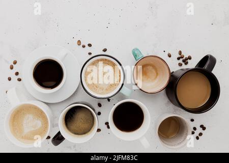 Draufsicht auf flachem Lay mit vielen verschiedenen vollen und leeren Kaffeetassen Zusammensetzung auf grauweißem Beton Hintergrund. Layout mit verschiedenen Teetassen. Getrocknete Kaffeebohnen. Espresso, Latte, Americano Stockfoto