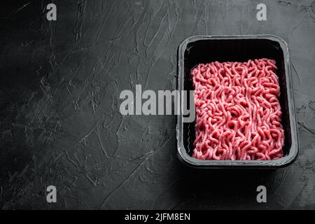 Rohes Hackfleisch in einem schwarzen Kunststoffbehälter auf schwarzem Steinhintergrund, mit Platz zum Kopieren von Text Stockfoto