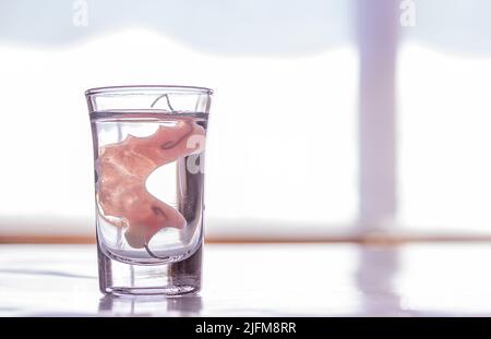 Close up Acryl Prothesen in ein Glas Wasser getaucht, Tisch im Schlafzimmer. Heller, einfacher Hintergrund. Stockfoto