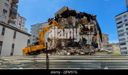 Großer gelber Bagger bricht altes Haus ab, Abriss eines Mehrfamilienhauses in einem Wohngebiet, Abriss einer Stahlbetonkonstruktion Stockfoto