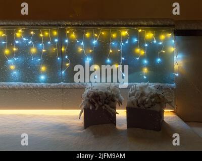 LED-Leuchten und eingeschneite, in Topf gegossene Heidekraut-Pflanzen auf einem Balkon oder einer Terrasse bei Nacht Stockfoto